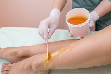 Güzellik uzmanı bir güzellik salonunda bir kadının bacaklarının şeker macununu tükürür. Kadın estetik kozmetolojisi.