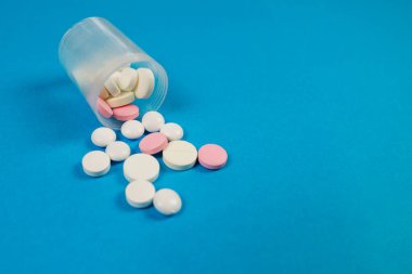 mavi arka planda farklı haplar ve ilaç şişesi