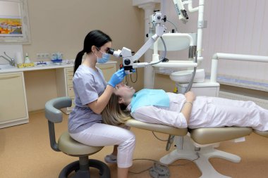 Mikroskop altında diş tedavisi. Kadın diş hekimi dişlerini diş kliniğinde mikroskop kullanarak tedavi eder.