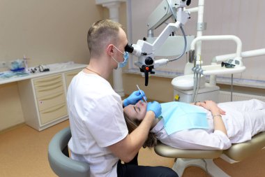 Mikroskop altında diş tedavisi. Erkek dişçi dişlerini diş kliniğinde mikroskop kullanarak tedavi eder.