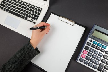 Ev ofisinin laptopu, panosu ve hesap makinesi olan bir iş yeri modeli. İş kadını panoya yazı yazıyor. Bir kadının eli kalemi tutar. Düz yatış, üst görünüm