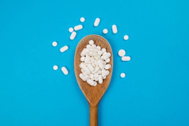 Tahta kaşıkta beyaz hapların en üst görüntüsü. Tıbbi konsept.