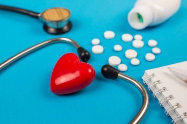 Tıbbi steteskop kırmızı kalp ve mavi arka planda haplar.