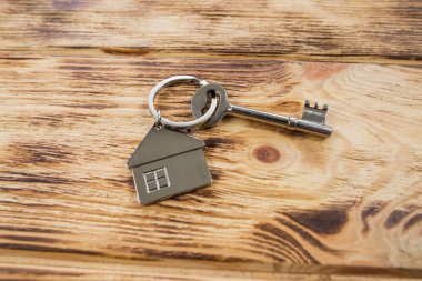 Ahşap arka planda bir ev şeklinde metal anahtarlık. Gayrimenkul, eve taşınma ya da emlak kiralama kavramları