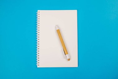 Beyaz bir defterin üst görünümü ve mavi arkaplanda bir kalem.