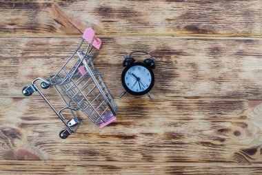 Küçük siyah çalar saat ve oyuncak alışveriş arabası, alışveriş arabasındaki saat, zaman kaybı, zaman kaybı, alışveriş zamanı.