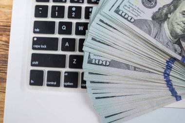 Dizüstü bilgisayarın arka planındaki 100 dolarlık banknotların üst görüntüsü. Bir dizüstü bilgisayar ve doların yakın plan parçası.