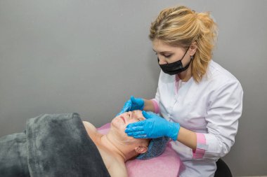 Güzellik uzmanı yetişkin bir kadının yüzünü temizlemek için oksijen maskesi takıyor. Spa salonunda cilt bakımı kavramı..