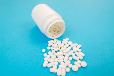 Plastik şişeden beyaz haplar döküldü. Mavi arka planda kapsüller. İlaç sanayisi. Eczacılık konsepti. Eczacılık ürünleri. Sağlık ve İlaç.