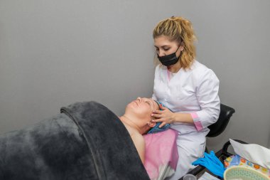 Yetişkin bir kadının yüzüne masaj yapan profesyonel bir güzellik uzmanı. Kaplıca salonunda cilt bakımı kavramı..