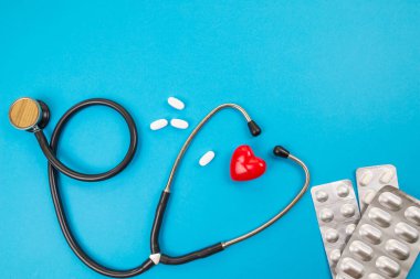 Sağlık konsepti, kardiyovasküler hastalık. Kırmızı kalp steteskopu ve mavi arka planda haplar..