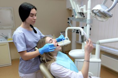 Dişçi. Diş beyazlatma. Doktor tedaviden sonra dişlerini muayene eder. Sağlıklı beyaz dişler. Kız dişçinin ofisindeki aynaya bakar.