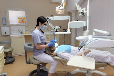Stomatoloji uzmanı profesyonel diş mikroskobu yardımıyla hastanın dişlerini inceler. Diş hekimi restorasyon aletleri kullanarak çürük önleme. Müşteri diş hekimi sandalyesinde yatıyor.
