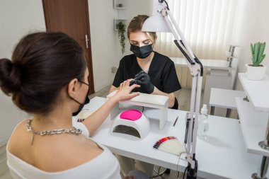 Güzellik salonunda lastik eldivenlerin ustası. Tırnaklarını vernikle kaplıyor. Mükemmel manikür süreci. Jel cilası konsepti. Tırnak bakımı
