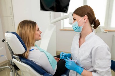 A female dentist is talking to a patient sitting in a dental chair. Dentist's consultation.