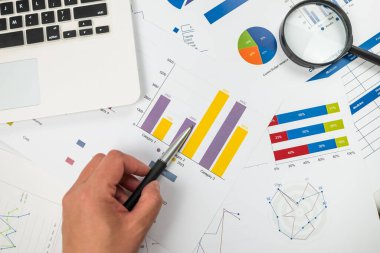 Çizelgeye işaret eden bir kadının yakın çekimi. İstatistiksel verileri karşılaştırır, grafik grafiklerindeki değerleri inceler, eğilimlerin örüntülerini analiz eder, notlar alır