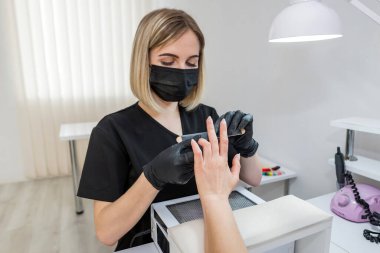 Manikür testeresinin ustası güzellik salonundaki tırnak uzatma işlemi sırasında tırnak şekli takıyor. Eller için profesyonel bakım.