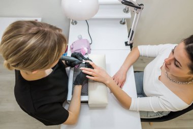 Kuaförde hırdavatçı manikürü. Usta, bir güzellik salonunda modemi kullanan bir kıza manikür yapıyor. Profesyonel tırnak bakımı kavramı. Yukarıdan görüntüle.