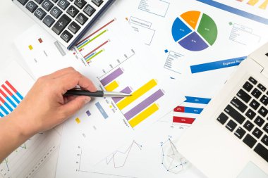 Çizelgeye işaret eden bir kadının yakın çekimi. İstatistiksel verileri karşılaştırır, grafik grafiklerindeki değerleri inceler, eğilimlerin örüntülerini analiz eder, notlar alır
