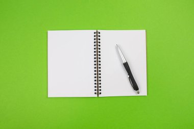 Yeşil zemin üzerinde bir kalem ile beyaz boş bir not defterinin üst görünümü.