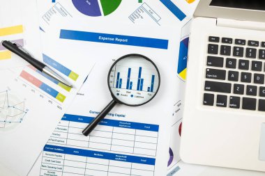 Büyüteç ve dizüstü bilgisayarlı çizelgelerin üst görüntüsü. Hesap tabloları, finansal kalkınma grafiği, banka hesapları, istatistik, ekonomi, veri analizi, yatırım analizi, borsa