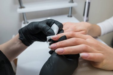 Manikürcünün ellerinin, müşterinin tırnaklarındaki süngerle yapışkan tabakayı çıkarması. Tırnaklarını mendille sil..