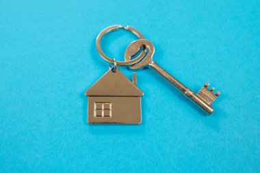 Mavi arka planda anahtarı olan metal anahtarlık. Ev şeklinde anahtarlık.