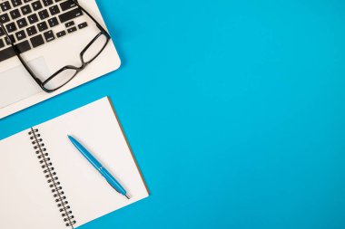 İzole edilmiş mavi bir arkaplanda dizüstü bilgisayar, kalem ve gözlük..