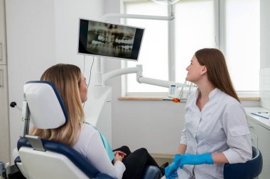 Kadın dişçi klinikte hastanın röntgenini gösteriyor.