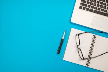 İzole edilmiş mavi bir arkaplanda dizüstü bilgisayar, kalem ve gözlük..