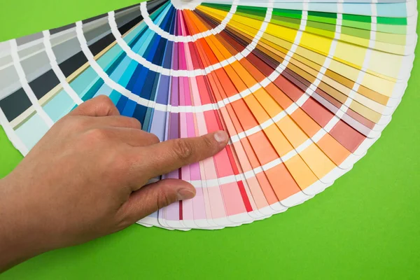 Female hand chooses color in palette swatches. Rainbow colors catalog isolated on green background