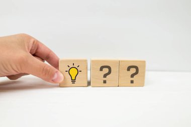 Yaratıcı fikir ve yenilik kavramı. Soru işareti ve ampul simgesiyle elle seçilen tahta küp bloğu