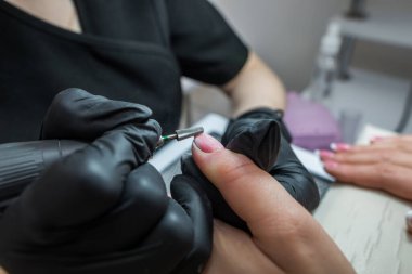 Manikürcü, jöle cilasını kesiciyle söker. Donanım manikürü yakın plan. Tırnaklarda Shellac kaplaması