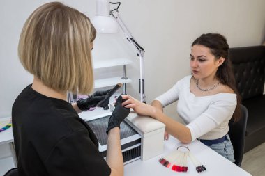 Manikür testeresinin ustası güzellik salonundaki tırnak uzatma işlemi sırasında tırnak şekli takıyor. Eller için profesyonel bakım.