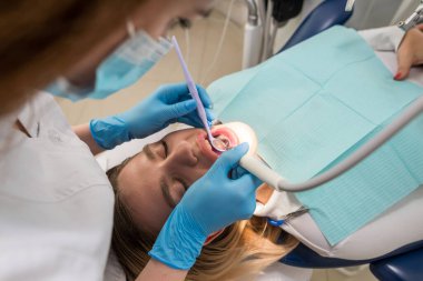 Dişçi-hijyenist, diş kliniğindeki bir kız için diş temizleme prosedürü uyguluyor. Tartarın çıkarılması. Diş hekimliği, diş tedavisi.
