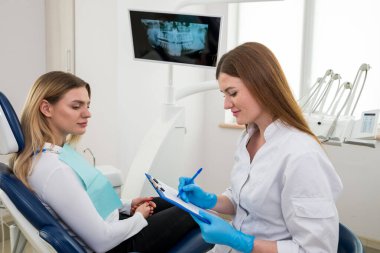 Hastalığın geçmişini saklayan diş hekimi, tedaviye başlamadan önce bir sandalyeye otururken hastadan bilgi talep eder. Dişçi, panoya bilgi yazar.