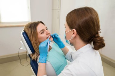 Diş hekimi, dişçi koltuğunda oturan genç bir hastanın dişlerini kontrol ediyor. Diş hekimi ve hasta muayenehanesinde. Diş tedavisi kavramı.