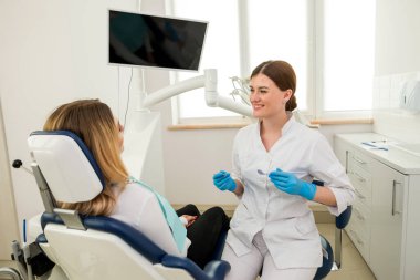 Güzel bir dişi dişçi bir sandalyede otururken bir hastayla konuşuyor. Açıklama, danışma, tavsiye, bir dişçinin tavsiyesi