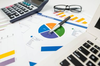 Kardaki büyüme ve azalma grafikleri. İş konsepti. İş aksesuarları (laptop, büyüteç, hesap makinesi, kalem, gözlük) ve grafikler, tablolar, ahşap ofis masasının üzerindeki diyagramlar. İstatistik, analiz kavramı