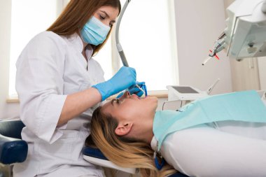 Dişçi-hijyenist, diş kliniğindeki bir kız için diş temizleme prosedürü uyguluyor. Tartarın çıkarılması. Diş hekimliği, diş tedavisi.