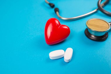 Tıbbi konsept. Steteskoplu kırmızı kalp ve mavi arka planda haplar..