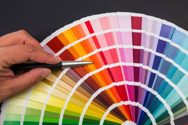 Kadın eli palet kumaş parçalarında renk seçer. Siyah arkaplanda izole edilmiş gökkuşağı renk kataloğu.