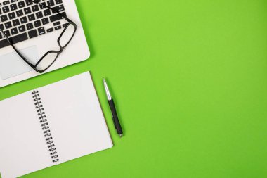 Yeşil arkaplanlı ve kopya alanı olan dizüstü bilgisayar gözlüklü not defteri üst görünümü.