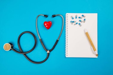 İzole edilmiş mavi arka planda kırmızı kalbin steteskop haplarının üst görüntüsü. Tıbbi konsept. Kardiyovasküler hastalıkların algılanması, sağlıklı kalpler..