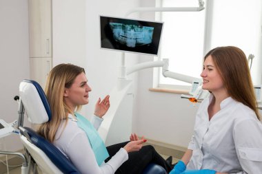 Güzel bir dişi dişçi bir sandalyede otururken bir hastayla konuşuyor. Açıklama, danışma, tavsiye, bir dişçinin tavsiyesi