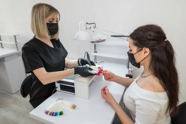 Tırnak rengi seçimi. Genç bir kız bir güzellik salonunda tırnaklarının rengini seçer. Tırnakların güzelliği ve sağlığı. Manikür ve manikür salonu müşterisi