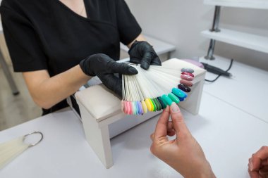 Tırnak rengi seçimi. Genç bir kız bir güzellik salonunda tırnaklarının rengini seçer. Tırnakların güzelliği ve sağlığı. Manikür ve manikür salonu müşterisi