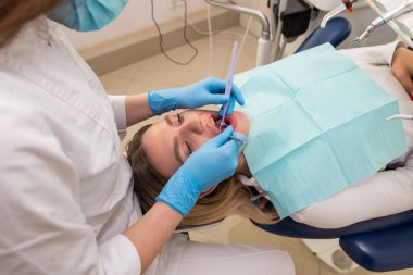 Dişçi-hijyenist, diş kliniğindeki bir kız için diş temizleme prosedürü uyguluyor. Tartarın çıkarılması. Diş hekimliği, diş tedavisi.