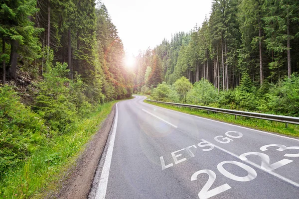 Let\'s Go 2023 written on the road in the forest.2022 New Year road trip travel and future vision concept . Nature landscape with highway road leading forward to happy new year celebration in the beginning of 2022 for fresh and successful start .