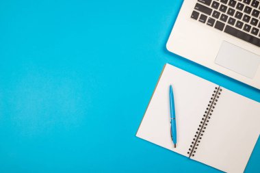 İzole edilmiş mavi zemin üzerinde not defteri ve kalemle beyaz dizüstü bilgisayarın üst görüntüsü. metin için boşluk kopyala.